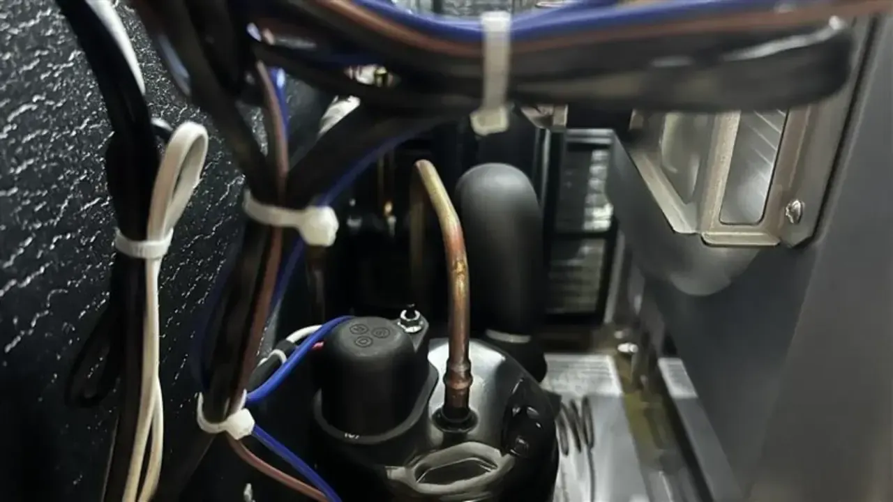 Copper tubing, wiring and the compressor area inside a refrigeration unit.