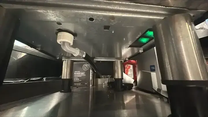 A view beneath a stainless-steel unit shows its supports, cable and illuminated switches.