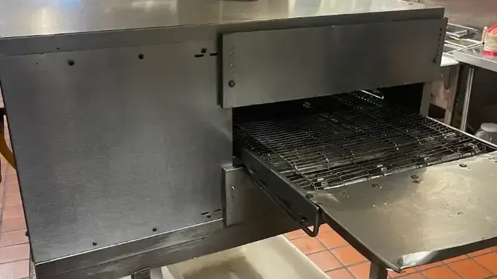 The conveyor belt and stainless-steel cooking chamber of a restaurant oven.